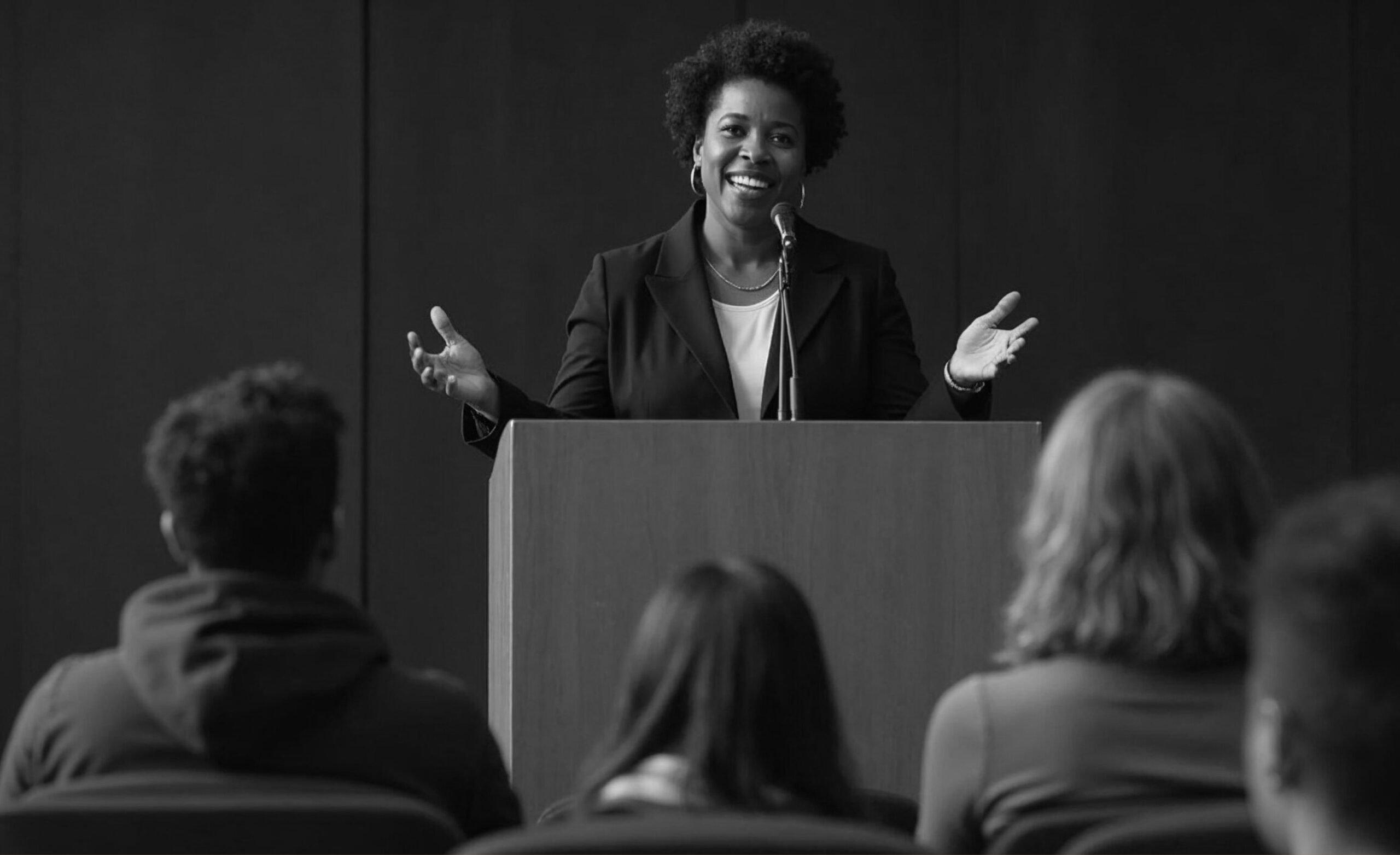 Female speaker addressing an audience at a podium, representing leadership in school communications and strategy.