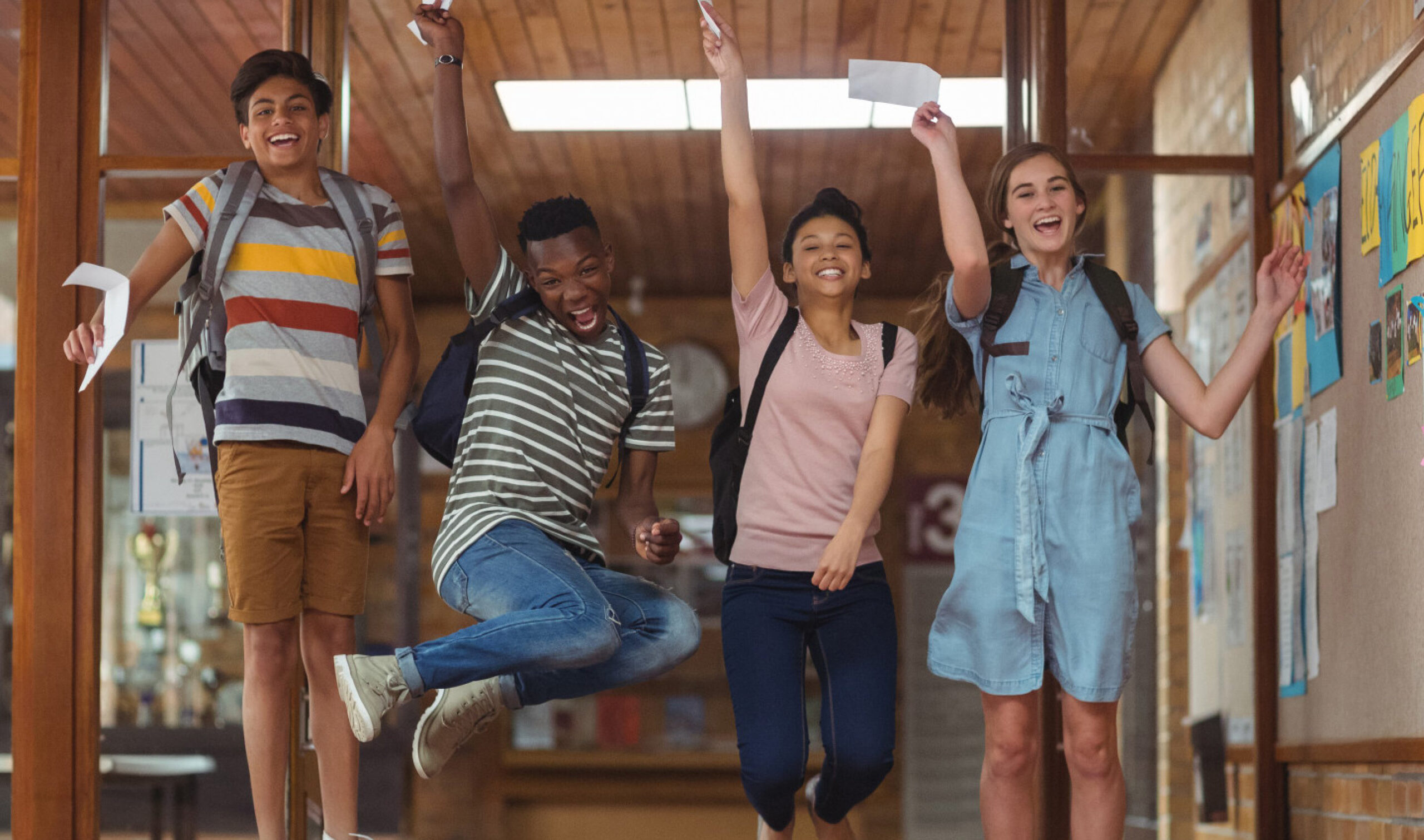 Happy students celebrating in a school hallway, representing positive student outcomes and the impact of effective school communications and strategy.